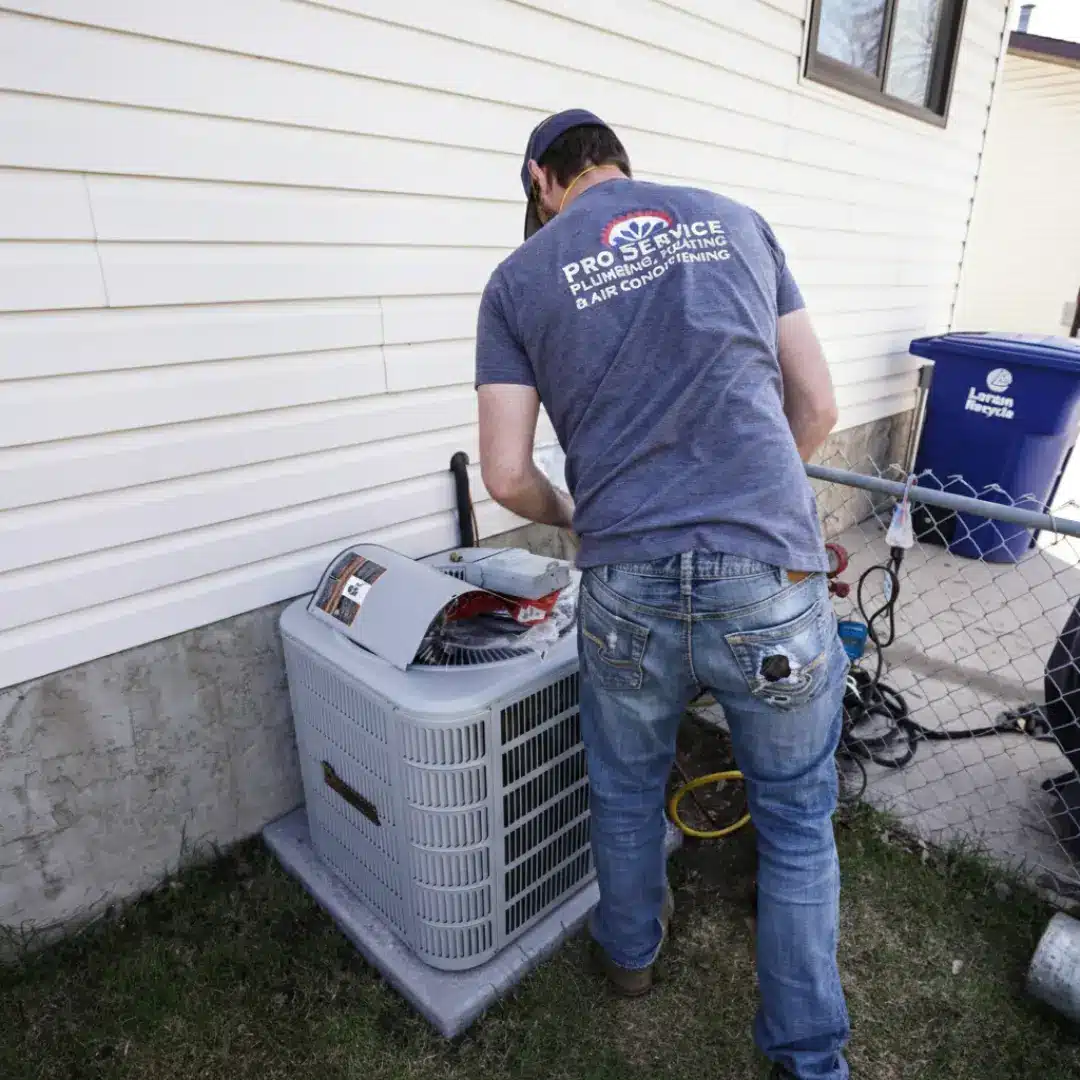 Pro Service Mechanical AC Condenser Installation Pro Service Mechanical technician servicing outdoor AC condenser unit with top panel removed at Saskatoon home